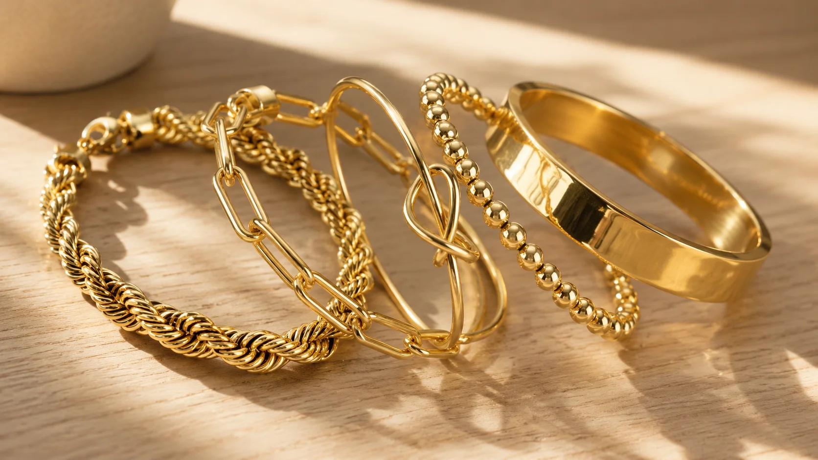 Close-up of various styles in stackable gold bracelets set including Cuban rope and paperclip chain